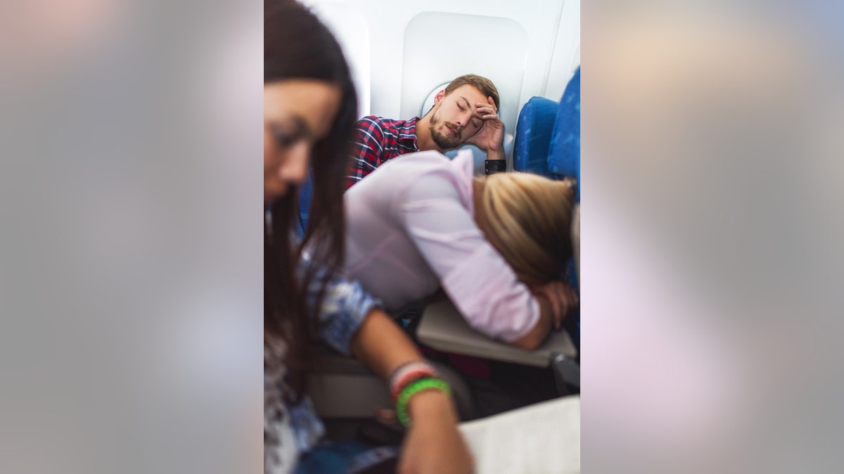 People traveling by airplane. Focus is on background, on young man sleeping.