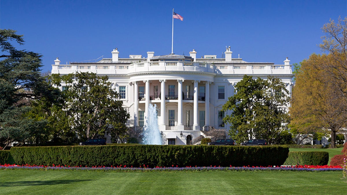 The South Portico of the White House. Washington DC. The White House is the official residence and principal workplace of the President of the United States, located at 1600 Pennsylvania Avenue. Beautifully landscaped lawn with flowers, fountain and blooming trees is in foreground. Deep blue clear sky is in background. American flag is flying atop. The image lit by spring evening sun. Canon 24-105mm f/4L lens.