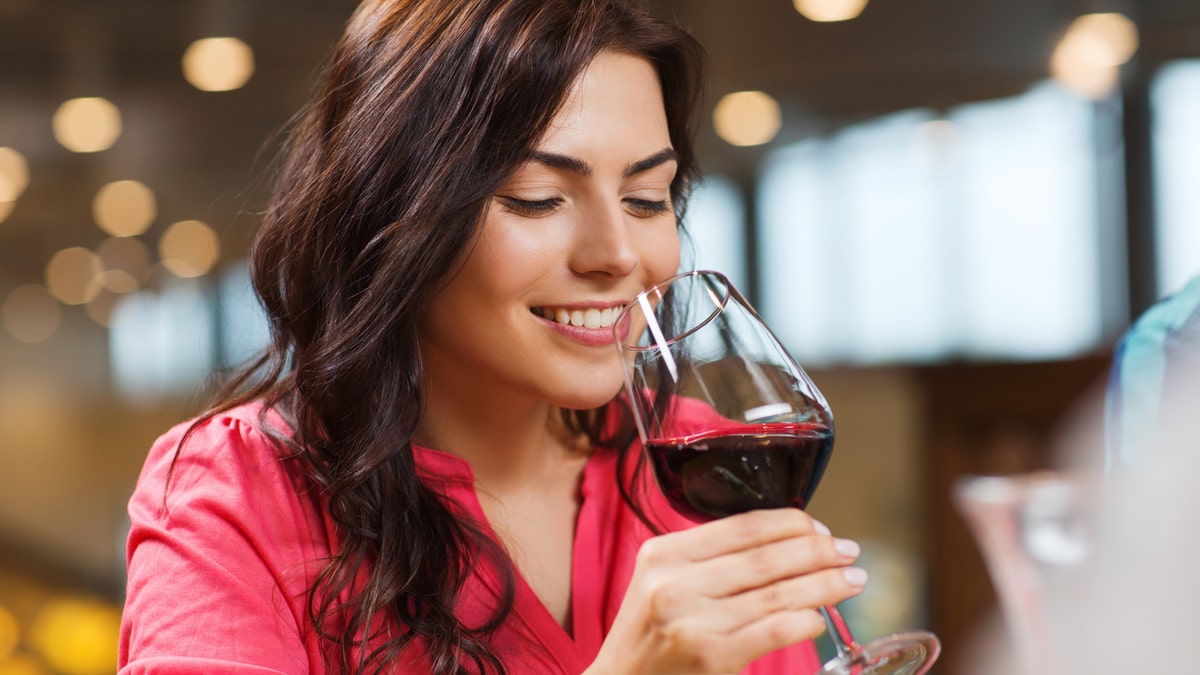 leisure, drinks, degustation, people and holidays concept - smiling woman drinking red wine at restaurant