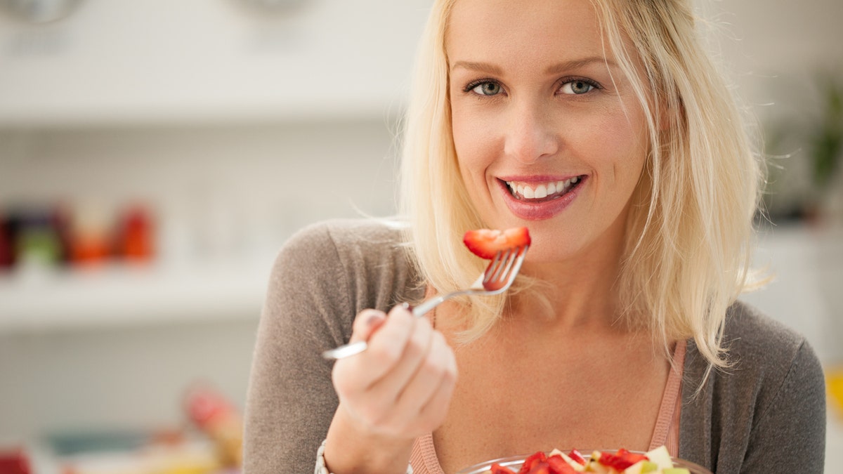 woman eating a fruit salad eating a strawberry istock