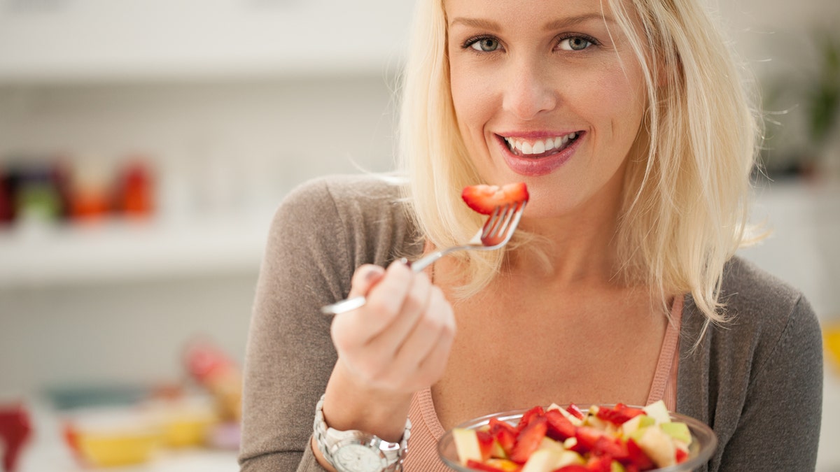 woman eating a fruit salad eating a strawberry istock