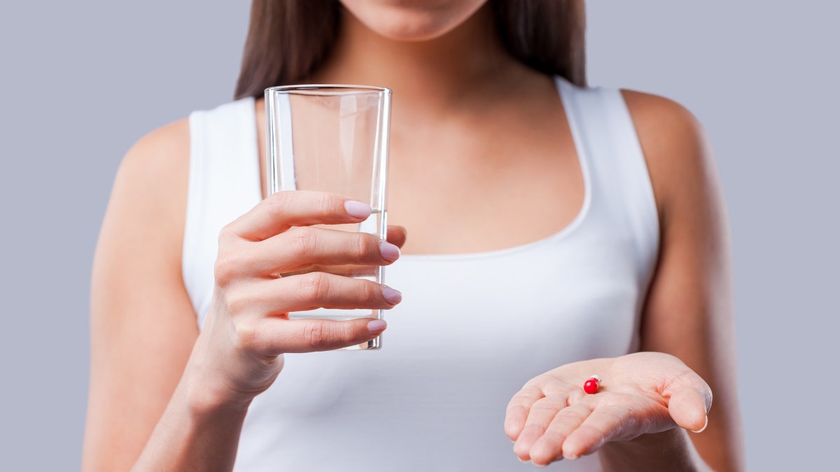 Cropped picture of young woman holding a glass with water and pills in her hands