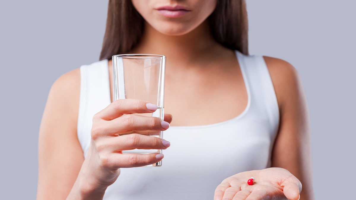 Cropped picture of young woman holding a glass with water and pills in her hands