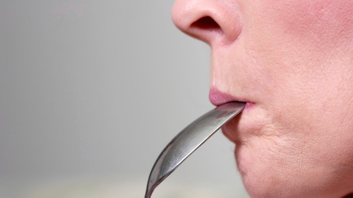 woman with spoon in mouth istock