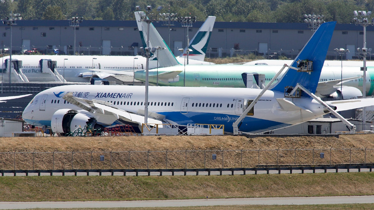 Workers on lifts are pictured near the tail of a Boeing 787-8 Dreamliner being built for Xiamen Airlines as a plane lands at Paine Field Airport in Everett, Washington August 7, 2014. Boeing has pushed some factory work on the 787 Dreamliner to the uncovered tarmac outside its assembly plant in Washington state in an effort to keep churning out the popular plane at a rate of one every three days, according to people with knowledge of the situation on August 8, 2014. Picture taken August 7, 2014. REUTERS/Jason Redmond (UNITED STATES - Tags: TRANSPORT BUSINESS) - GM1EA890BNE01