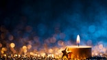 Tea light and a golden star on defocused blue and gold background.
