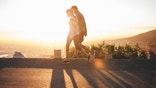 Couple walk along road at sunrise. Couple talking a walk on hillside road with bright sunlight.