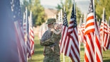 3 year old  girl running with her military dad who is wearing an American Army uniform in a field of American flags.