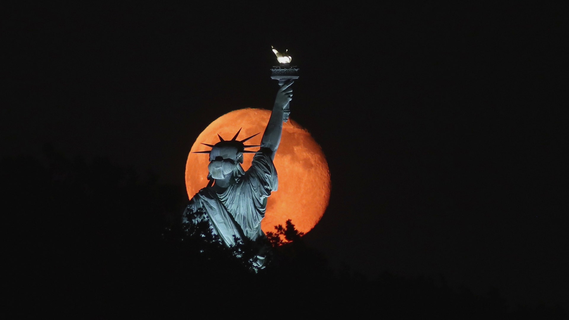 The moon rises behind the Statue of Liberty Sunday night as seen from Liberty State Park in Jersey City, NJ