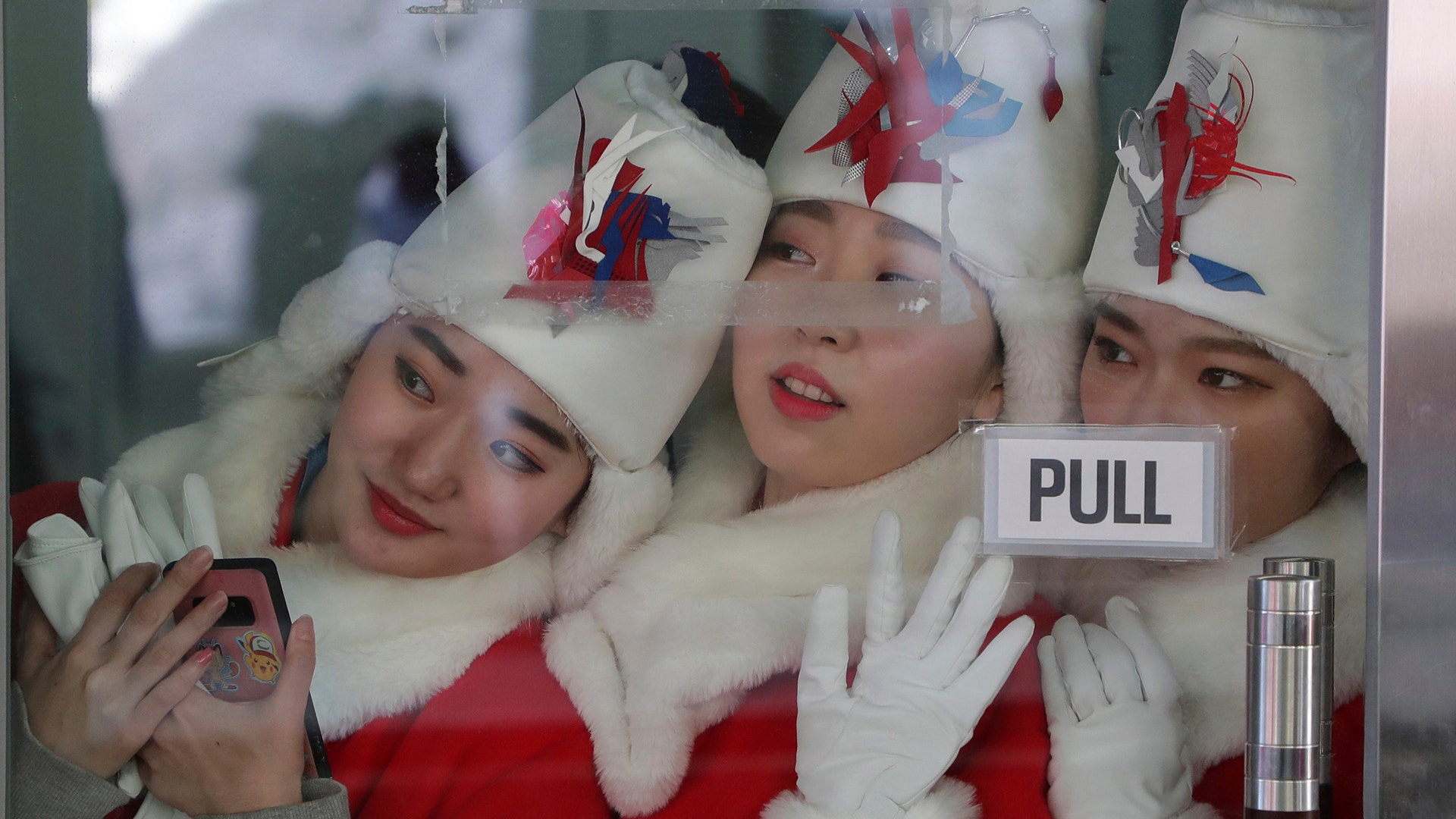The women who hand out the awards for the victory ceremony watch the sliders during the men's skeleton final at the 2018 Winter Olympics