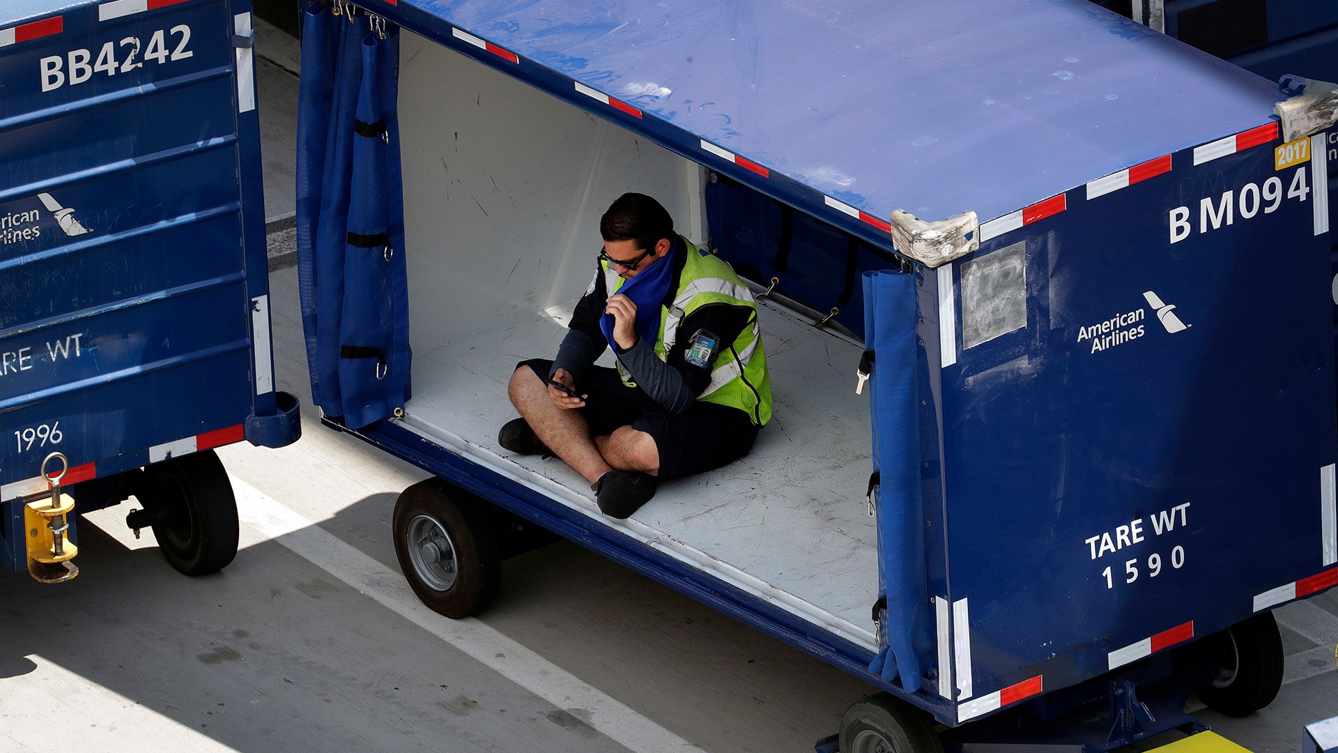 An American Airlines grounds crew member sits in a luggage cart at Sky Harbor International Airport to avoid the heat in Phoenix, Tuesday