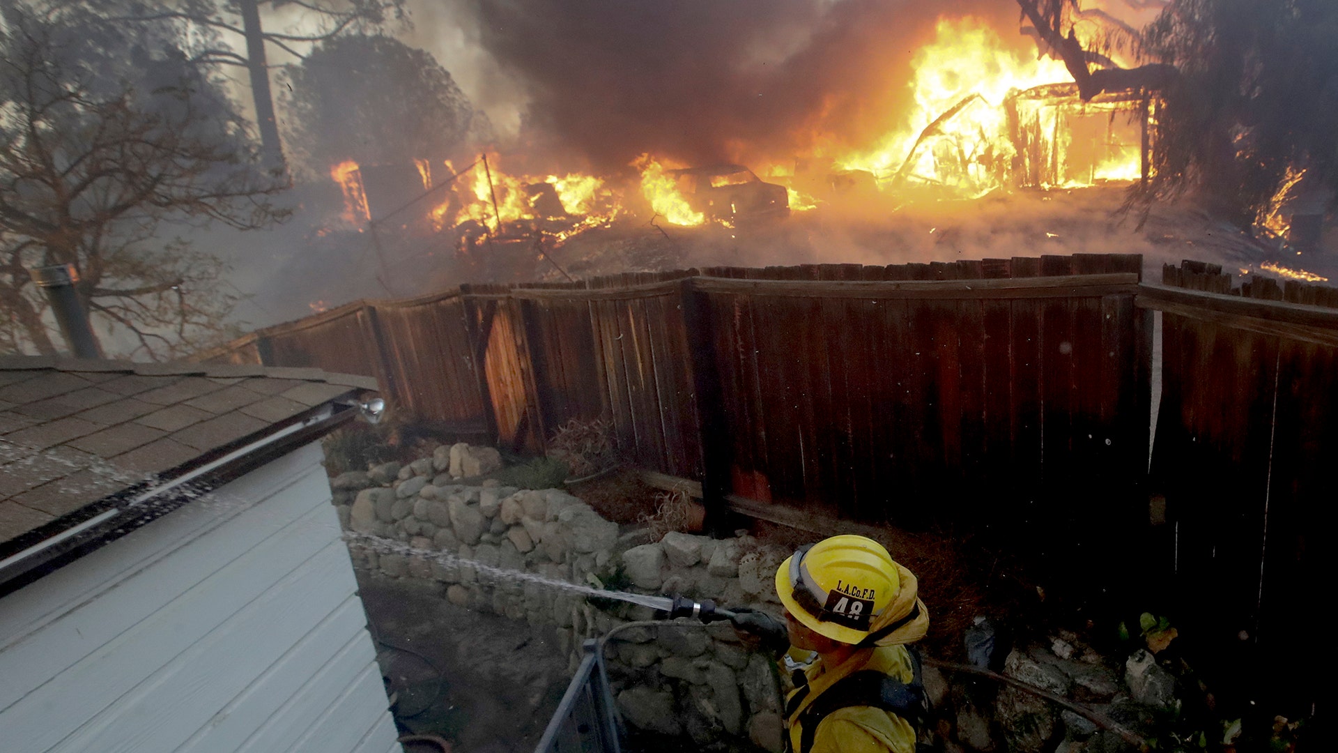 A Los Angeles County firefighter puts water on a burning roof during a wildfire in the Lake View Terrace area of Los Angeles, Tuesday