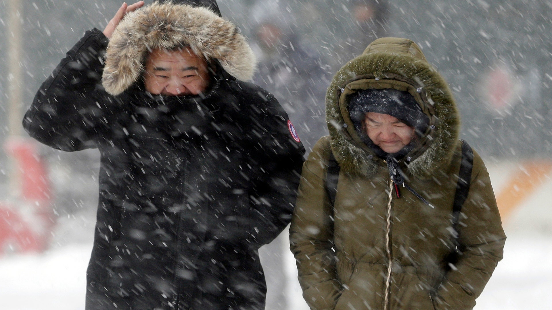 Pedestrians try to shield themselves as a strong wind blows snow in their faces in New York City, Thursday