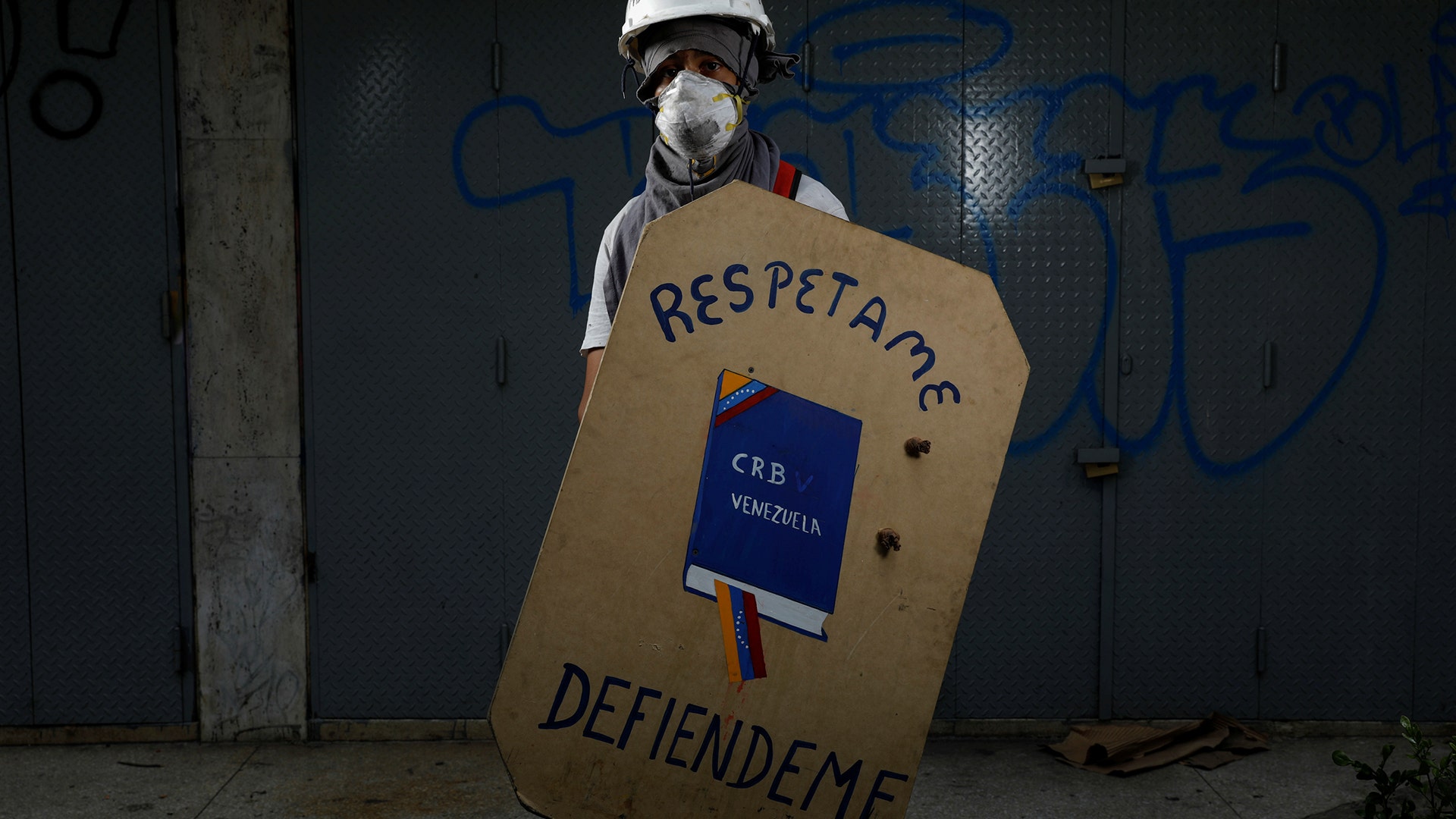 A demonstrator holding a shield that depicts the Venezuelan Constitution and reads