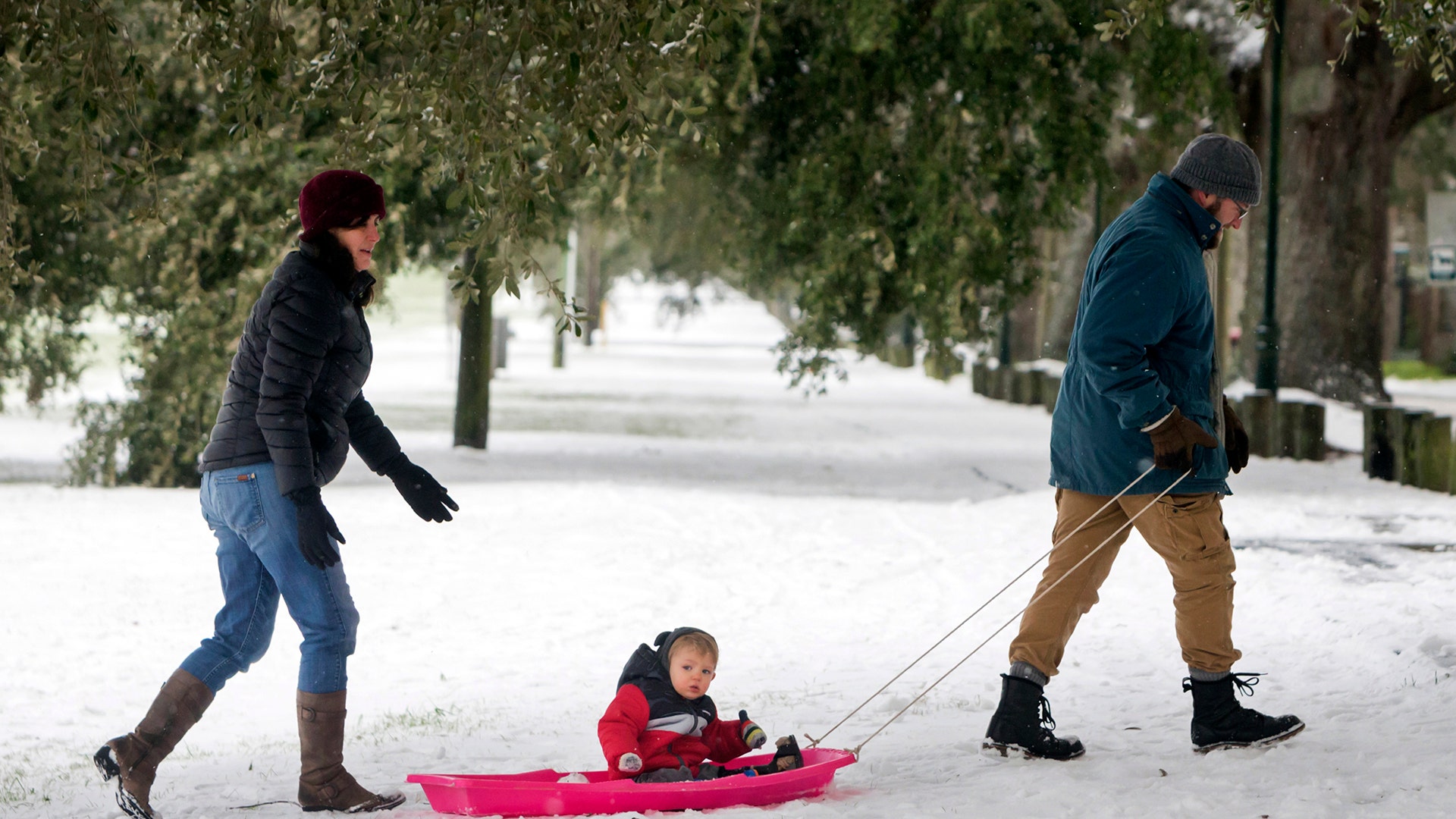 Debra Zumstein, left, and Will Kazary, right, push their son Alexander Kazary on a sled in a park, Wednesday, Jan. 3, 2018, in Savannah, Ga