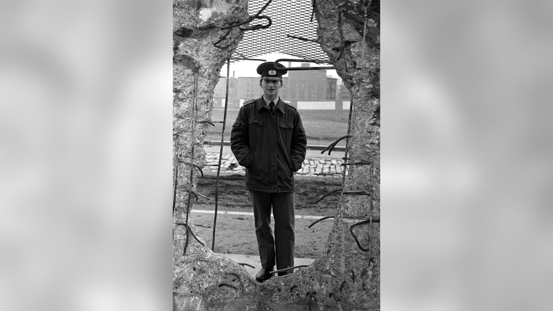 An East German border soldier looks through a large hole into the Berlin Wall, February 8, 1990