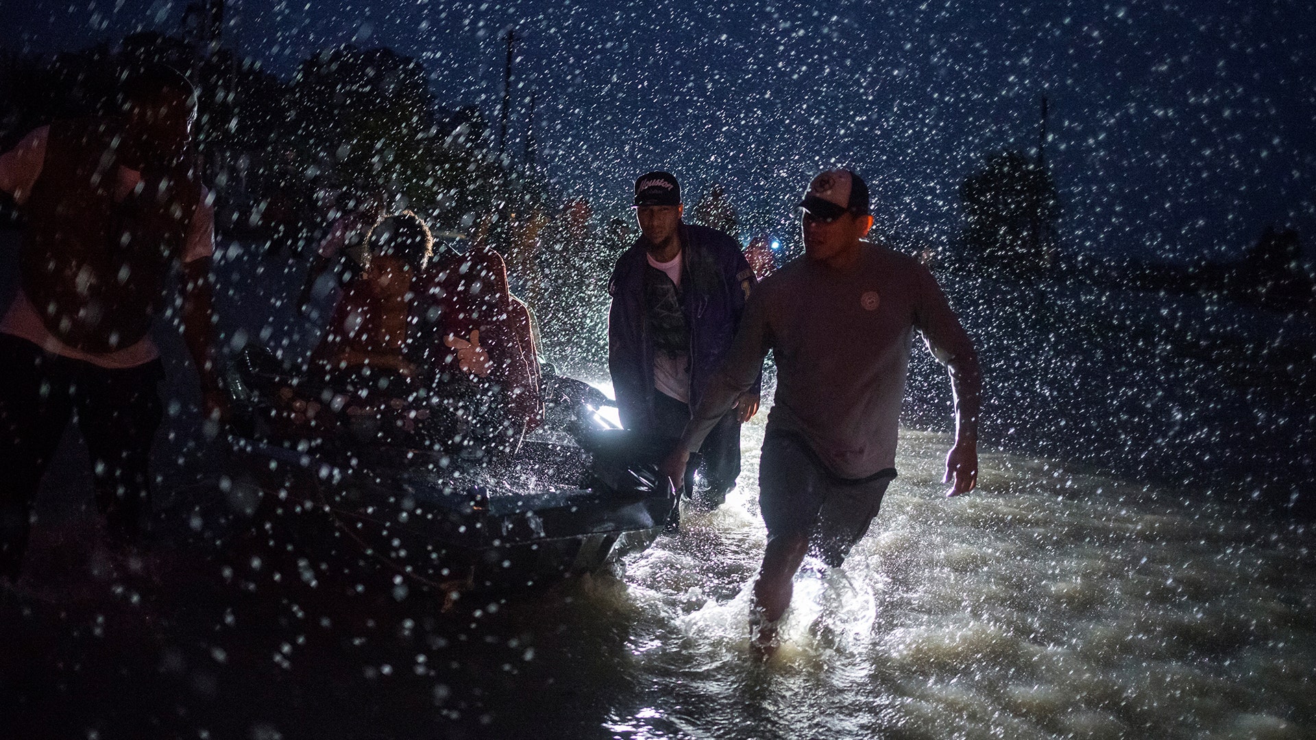 People help push a boat with evacuees to high ground along Tidwell Road in east Houston, Monday