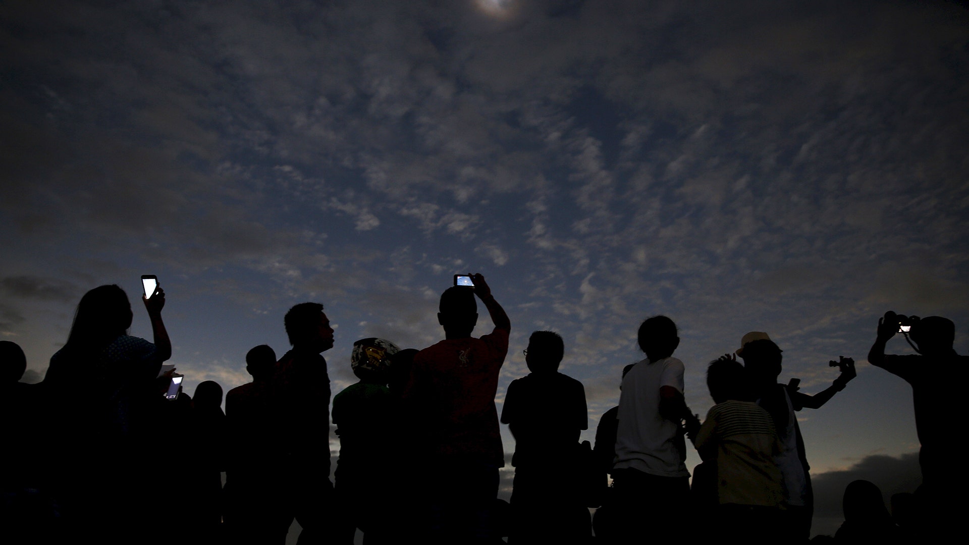 People watch and take pictures of the solar eclipse on the beach on Ternate Island, Indonesia, March 9, 2016