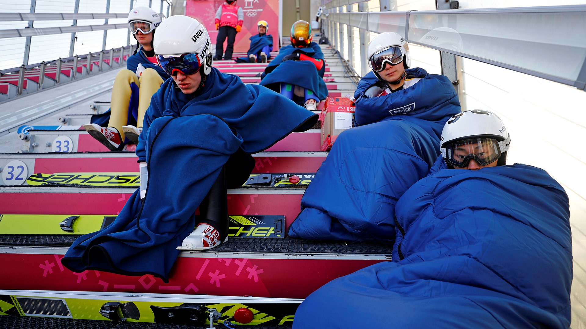Forerunners and athletes warm up as they wait for nordic combined ski jumping training to begin at the 2018 Winter Olympics