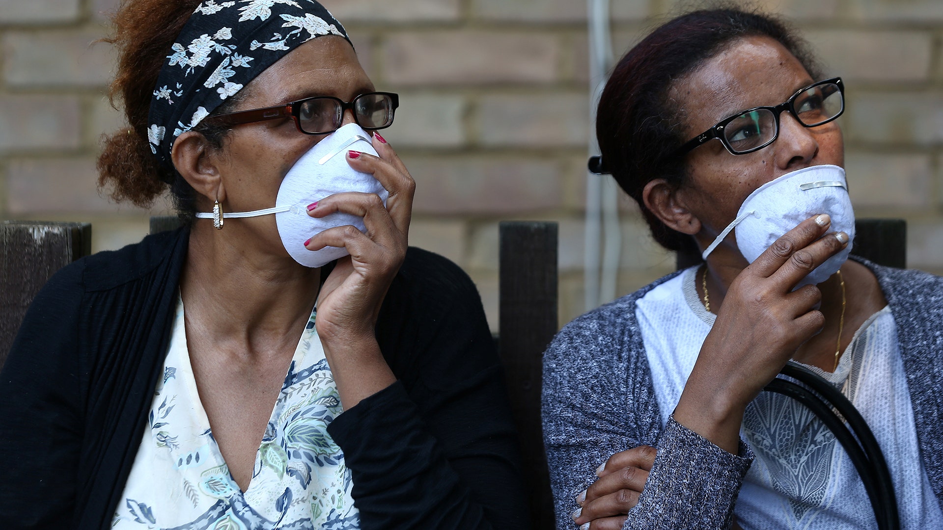 People wear masks near the apartment building fire, in West London