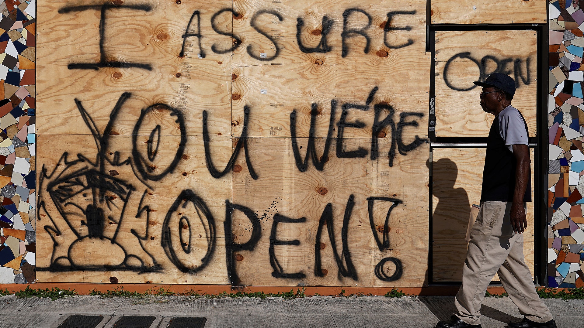 A man walks past a business that is open but boarded up in advance of Hurricane Irma's expected arrival in North Miami Beach, Thursday