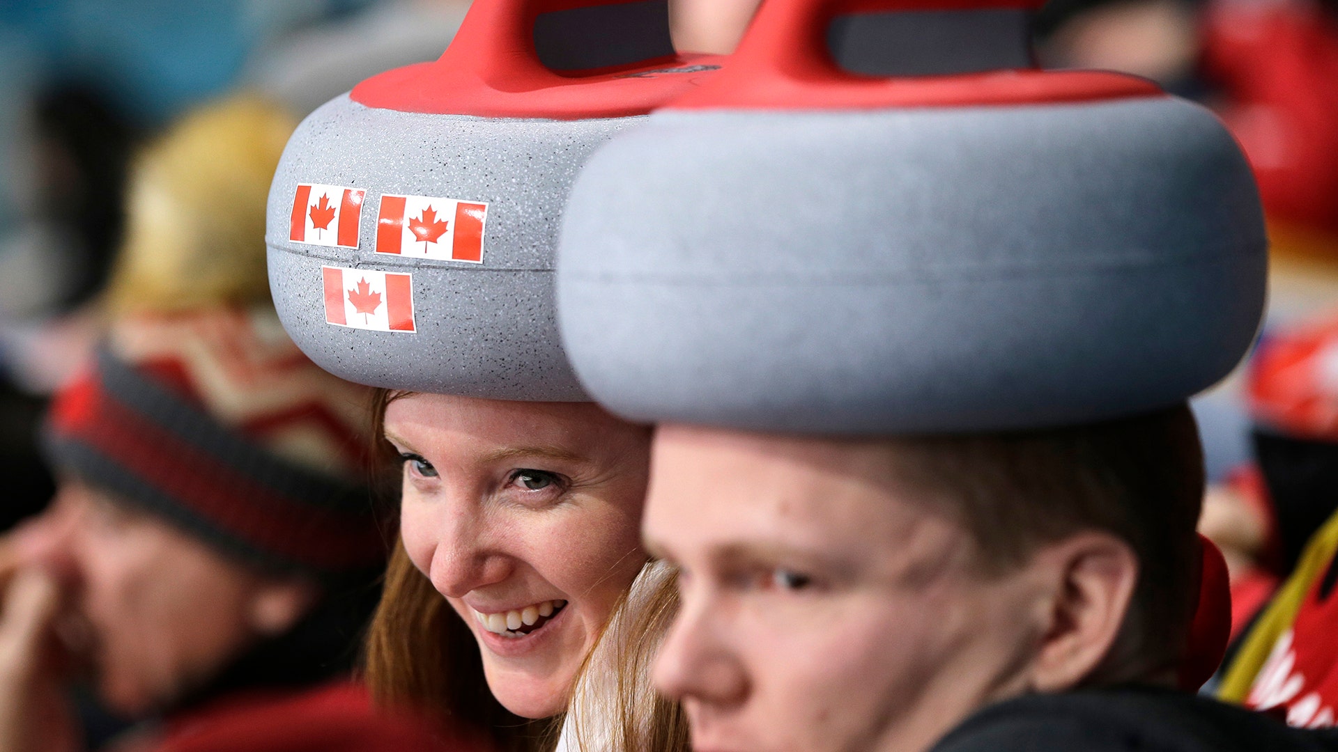 Spectators sport headwear shaped as curling stones as they watch the mixed doubles curling finals match at the 2018 Winter Olympics