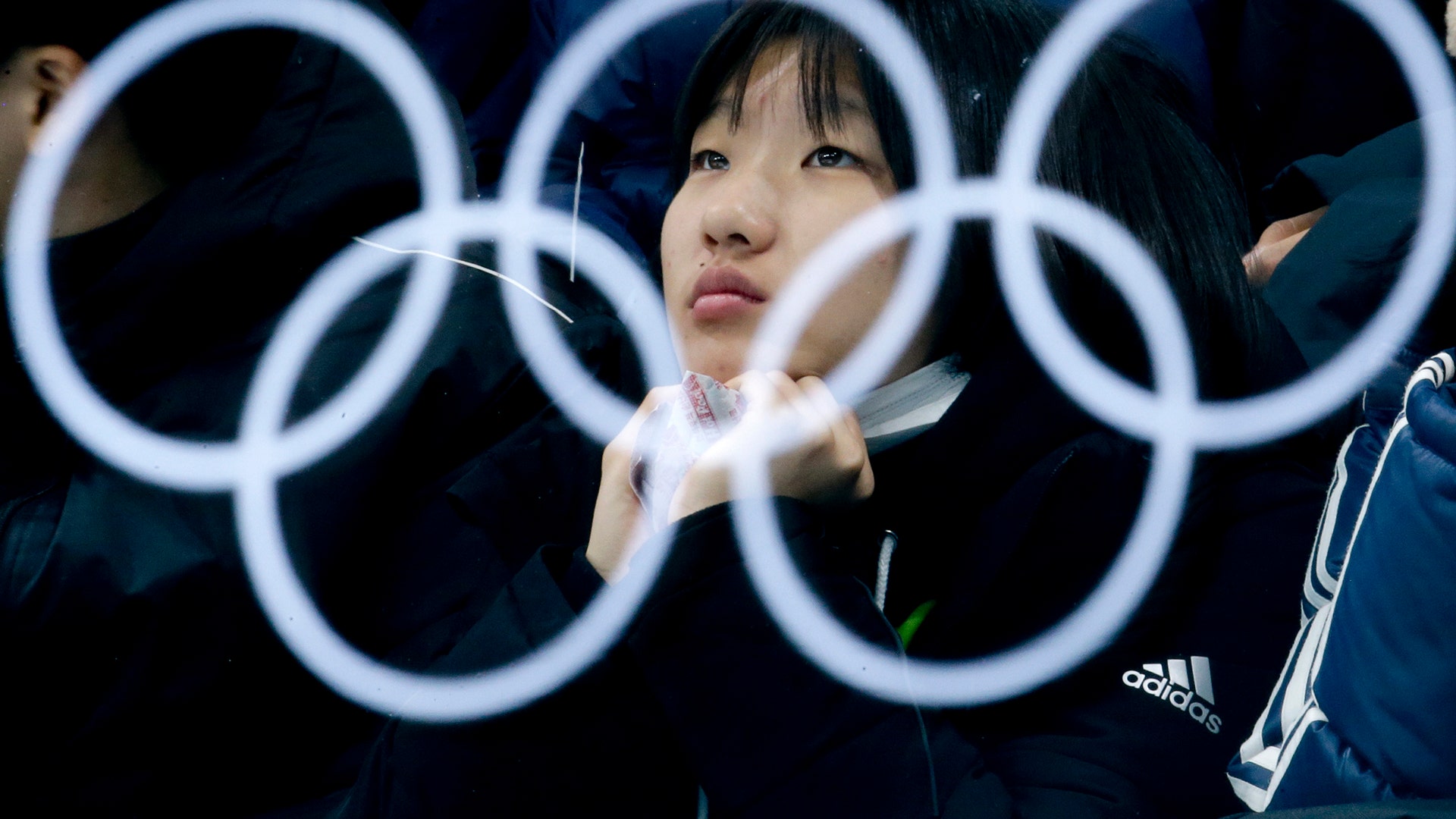 The Olympic rings are reflected in glass as a spectator watches the mixed doubles semi-final curling match between Canada and Norway