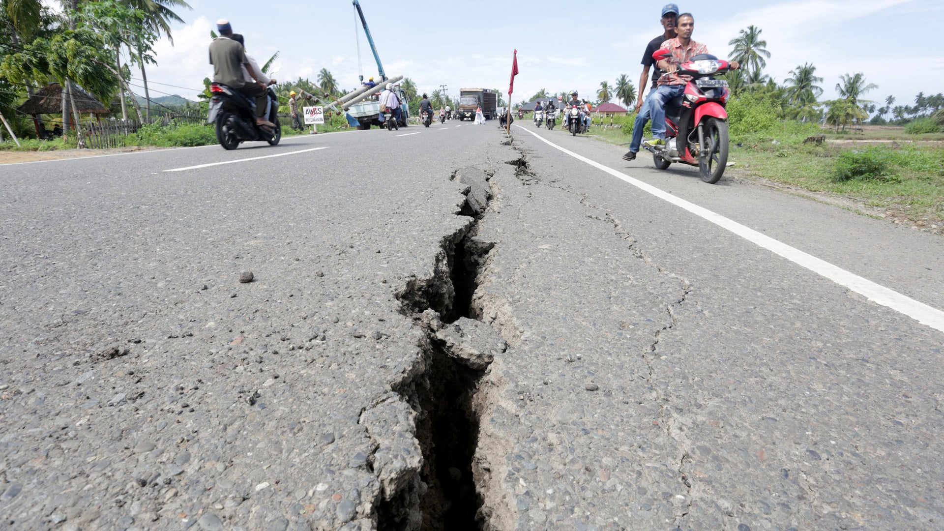 Motorcyclists pass a damaged section of a road following an earthquake in Meuredu, Pidie Jaya, in the northern province of Aceh, Indonesia.