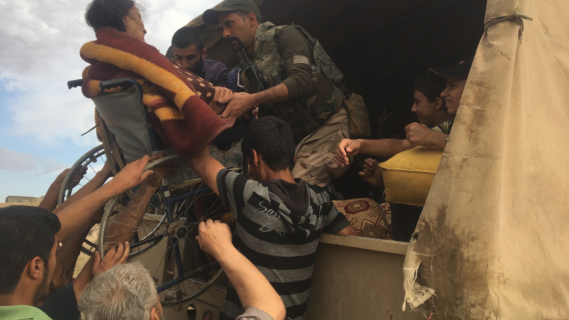 An Iraqi Medic and civilians lift an elderly lady in a wheelchair into the back of a transport truck, May 5, 2017