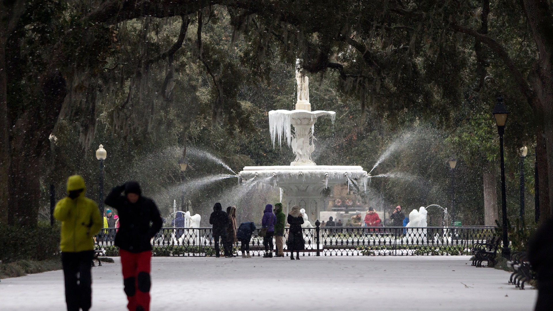 Visitors walk around the frozen fountain and snow covered sidewalks at Forsyth Park, in Savannah, Ga