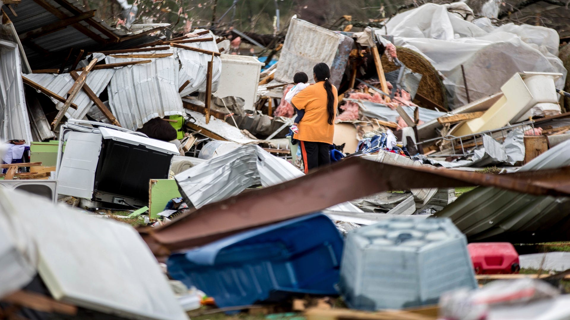A woman holds a child while walking through a farm that was damaged by a tornado, Sunday, Jan. 22, 2017, in Adel, Ga.