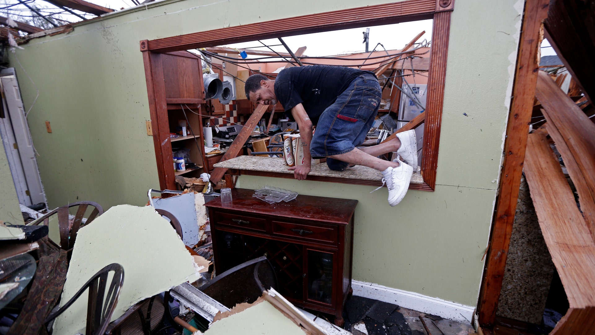Gregory Rugon climbs out of his home after failing to find his glasses that he lost taking cover after the tornado.