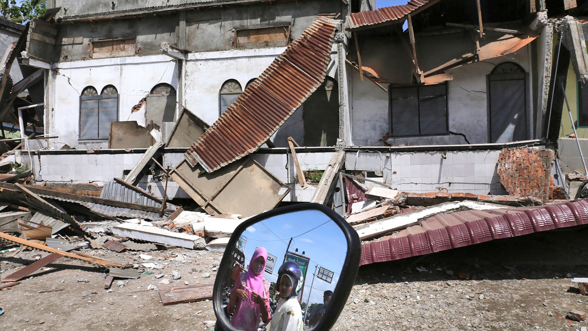 Women are reflected in a motorbike's mirror as they access the damaged building after an earthquake in Pidie Jaya, Aceh province, Indonesia.