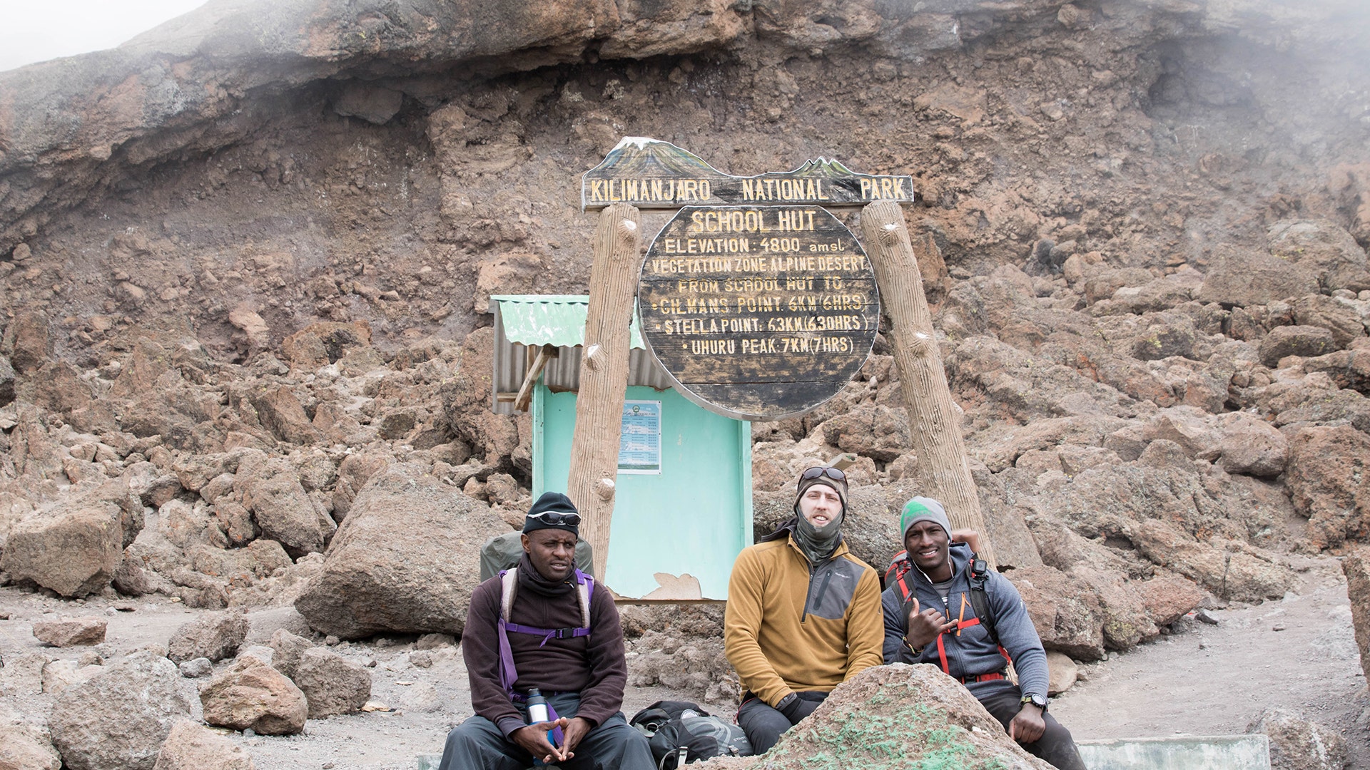 Jake Rath, middle, and Marine veteran Cpl. Kionte Storey sit with one of their guides during the climb up Mount Kilimanjaro.