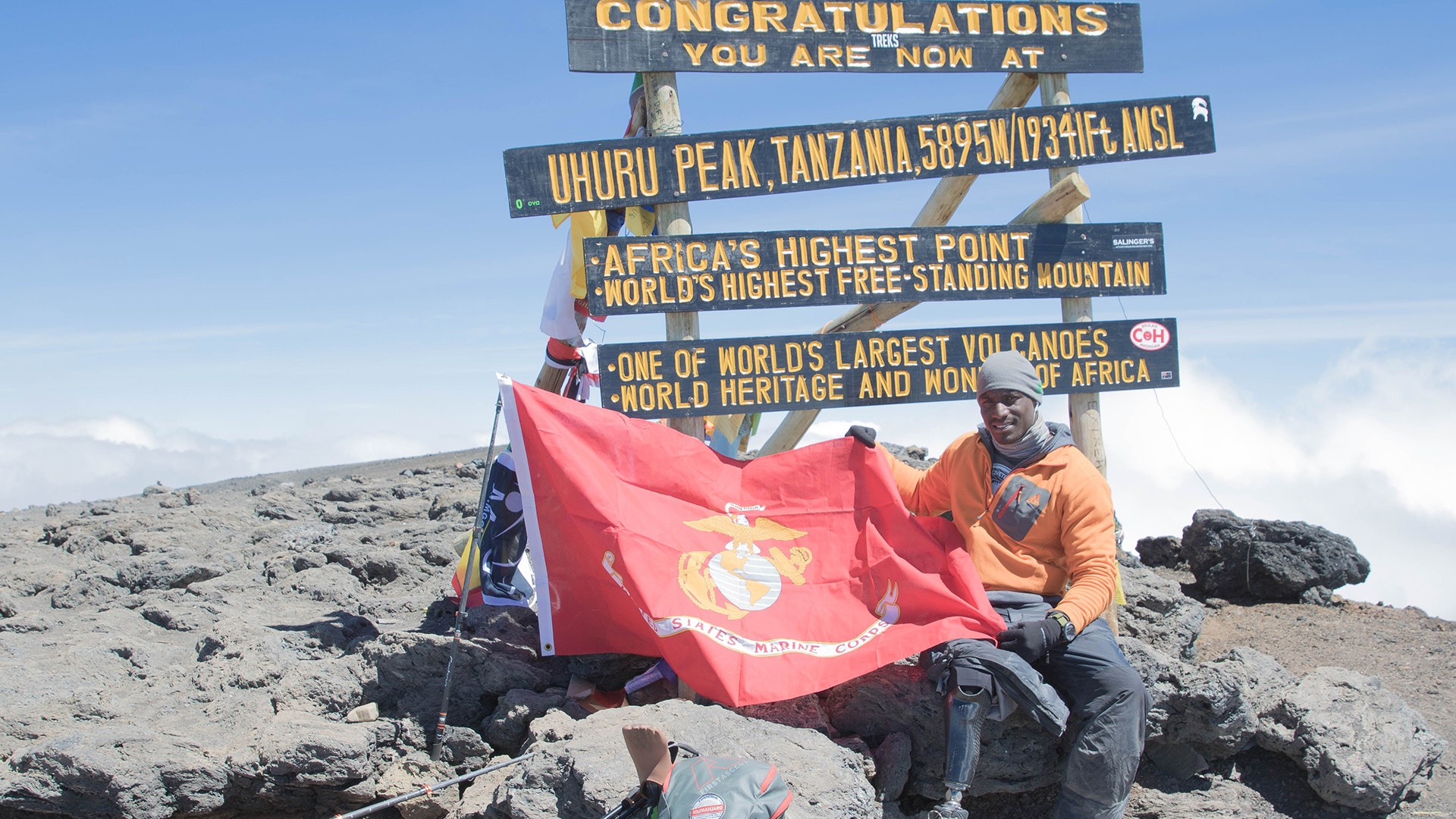 Marine veteran,Cpl. Kionte Storey at Uhuru Peak the summit of Mount Kilimanjaro at 19,341 feet, with a Marine Corps flag.