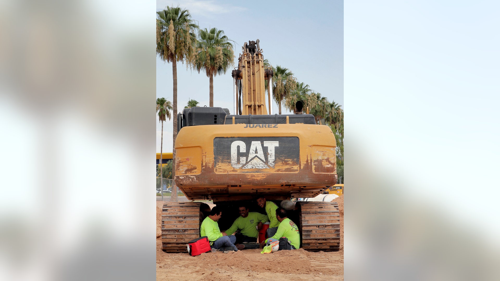 A crew from Juarez Construction sits under their excavator during a break to avoid the heat in Tempe, Tuesday