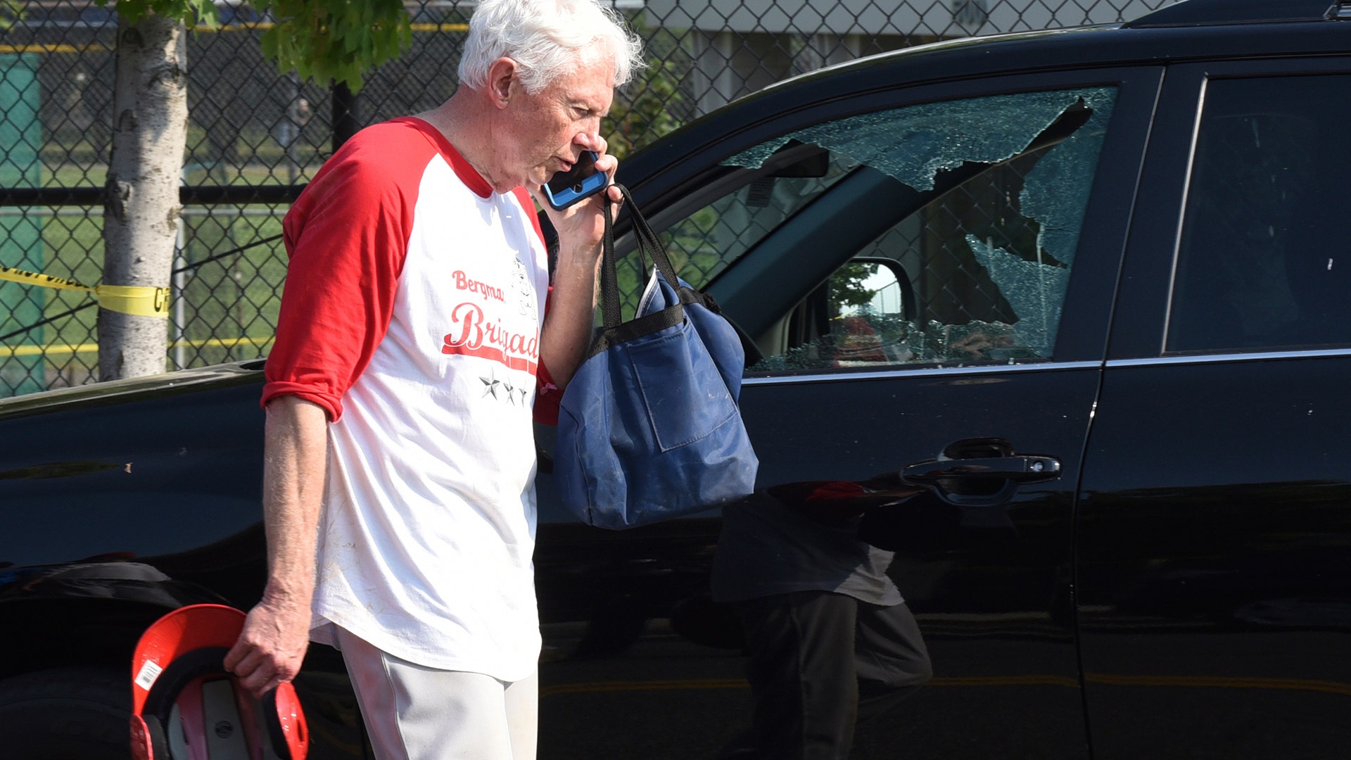 Rep. Jack Bergman, R-Mich. talks on the phone while walking past a damaged vehicle at a shooting scene