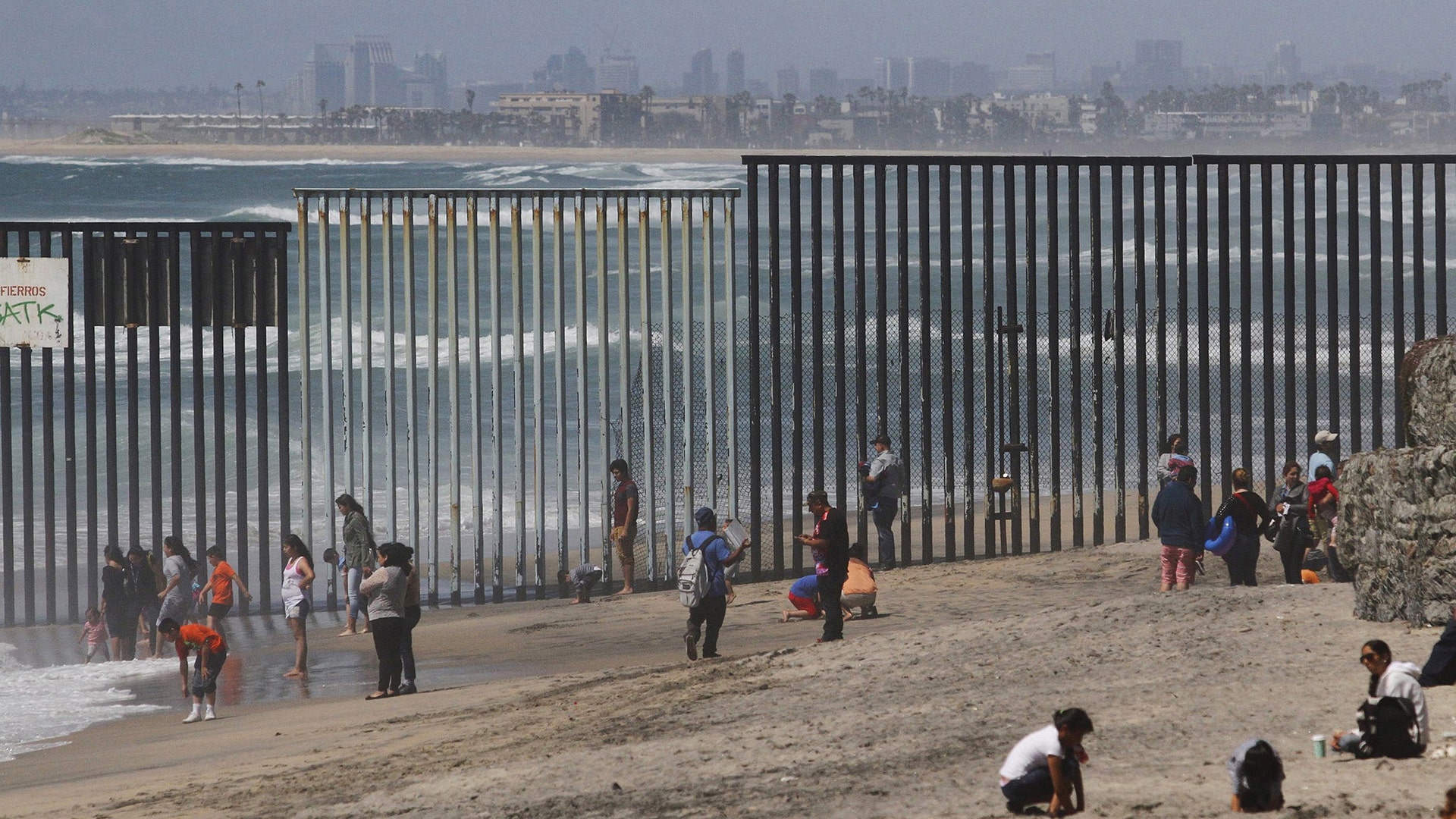 People are seen next to a wall separating Mexico and the United States, as photographed from Playas Tijuana, in Tijuana, Mexico.