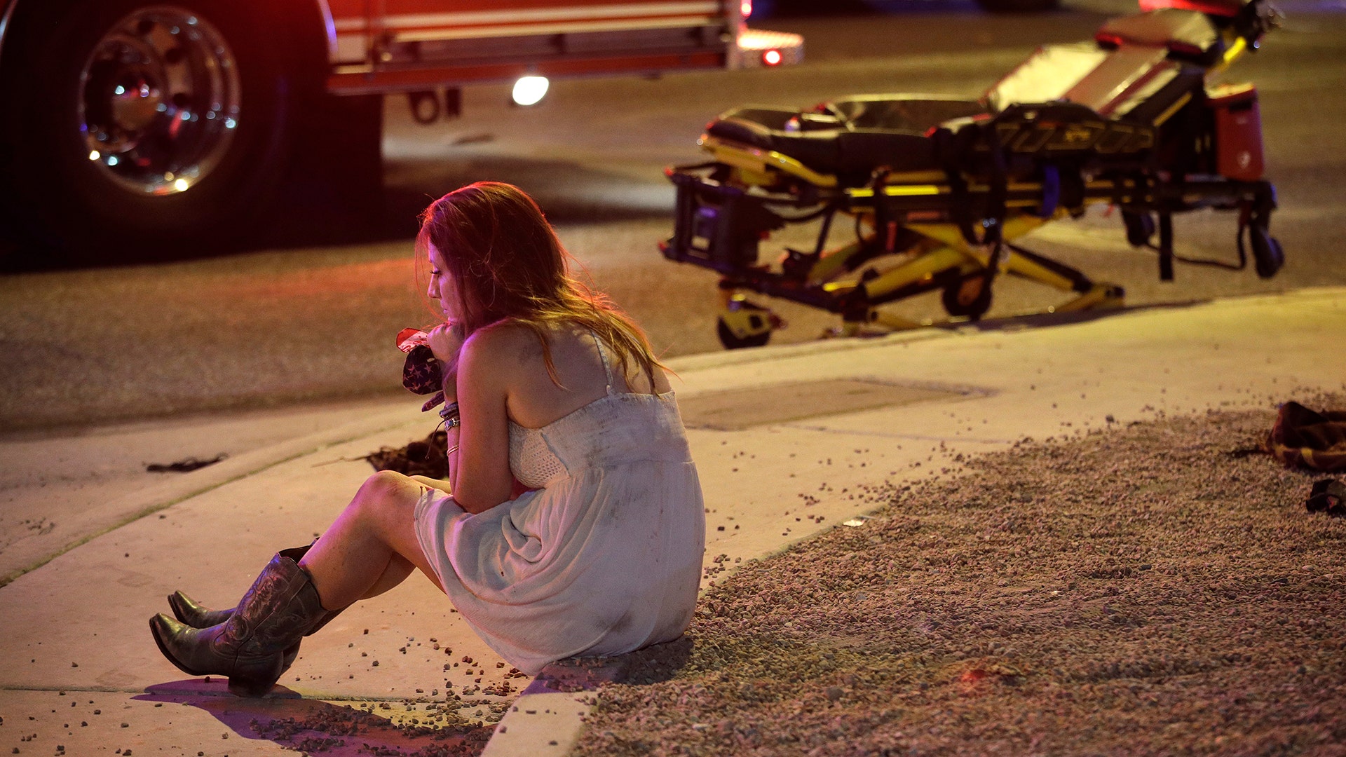 A woman sits on a curb at the scene of a shooting outside of a music festival along the Las Vegas Strip, Sunday
