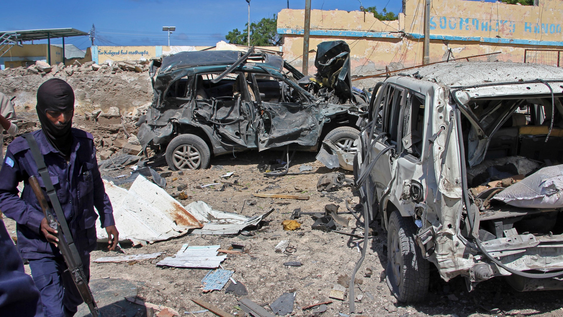 A Somali soldier walks past destroyed vehicles at the scene of a car bomb attack in Mogadishu, Somalia