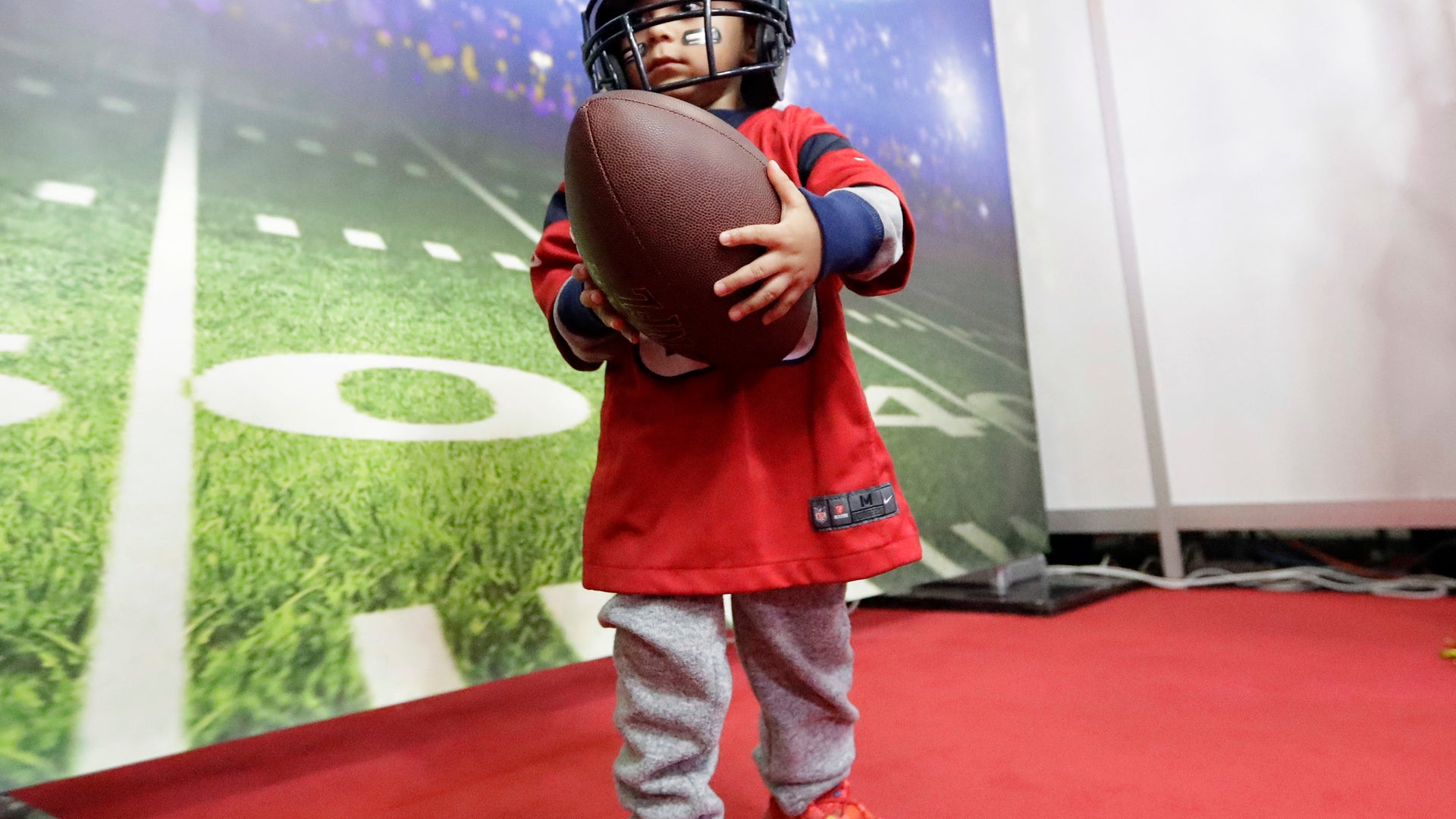 Jesus Cardenas Jr., 2, carries a football as he walks through an exhibit at the NFL Experience.