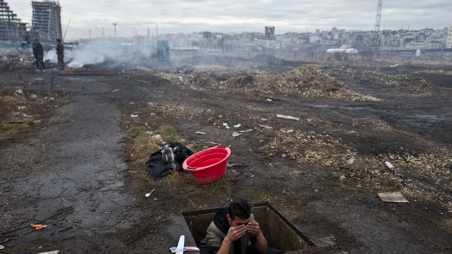 An Afghan refugee youth washes himself in a hole in the ground outside an old train carriage where he and other migrants took refuge in Belgrade, Serbia.
