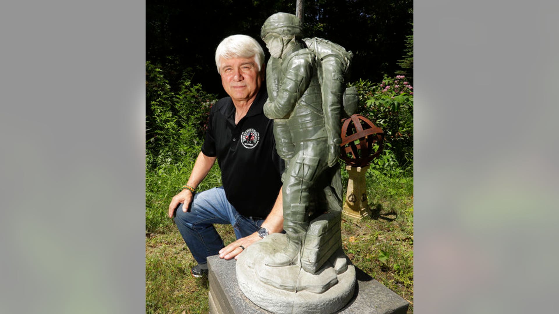 Former Army medic James McCloughan kneels next to a statue presented to him by a fellow soldier in South Haven, Michigan