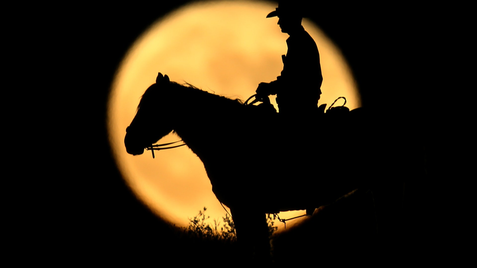 A full moon rises behind U.S. Border Patrol agent Josh Gehrich as he sits atop a hill while on patrol near Jacumba, California.