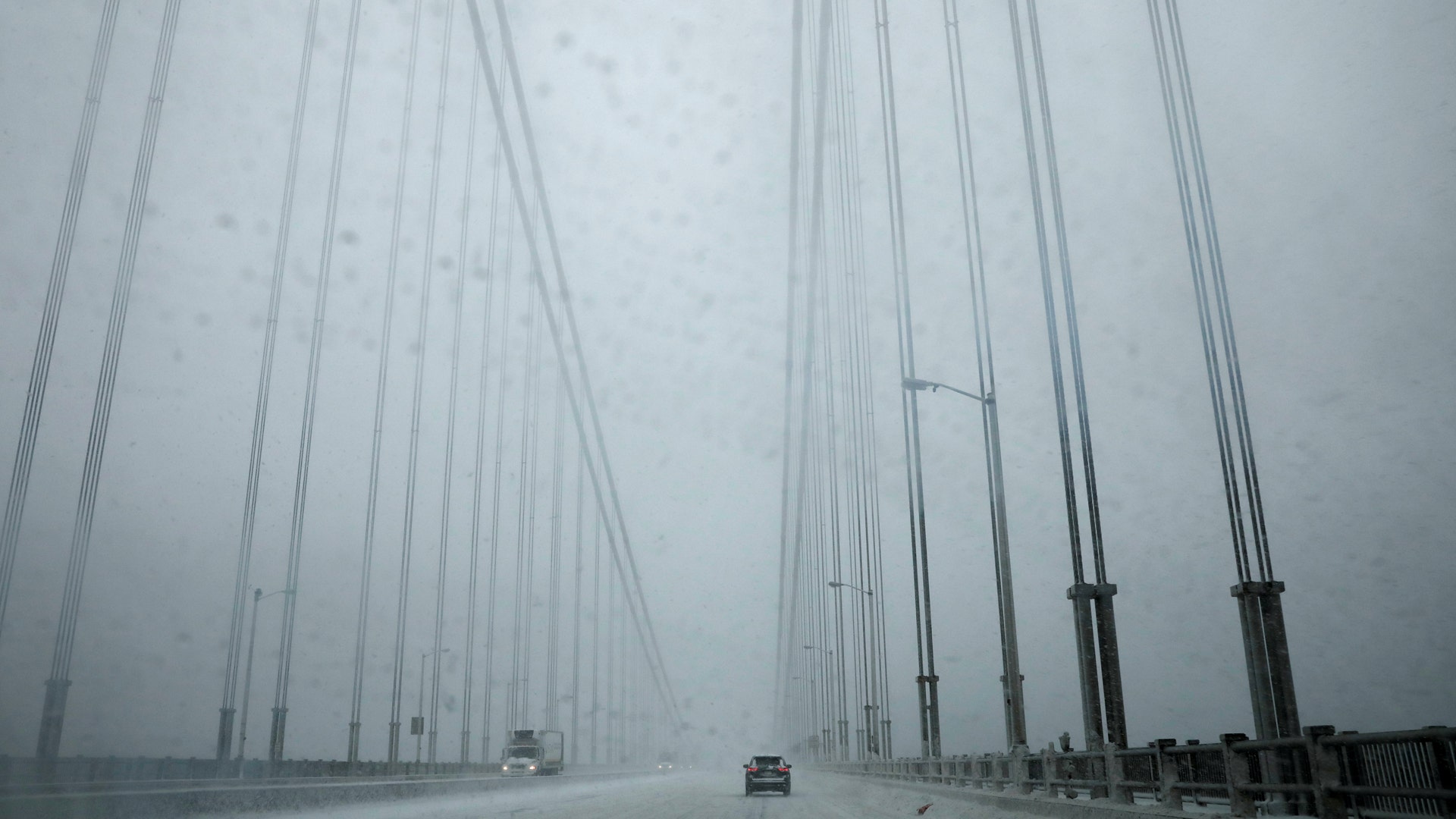 A car travels across the George Washington Bridge from New Jersey towards New York City in heavy falling snow.