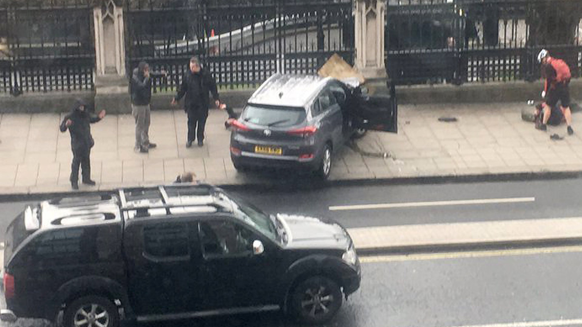 People stand near a crashed car and an injured person lying on the ground.