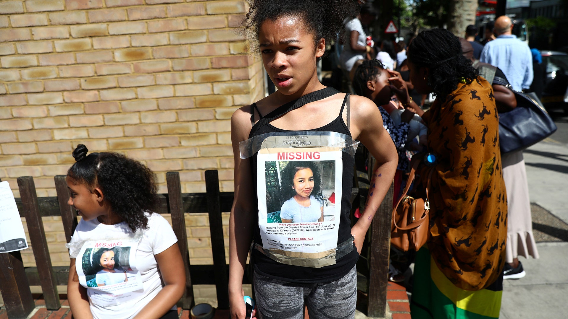 Missing person posters are worn by people standing near the apartment building destroyed in a fire in London