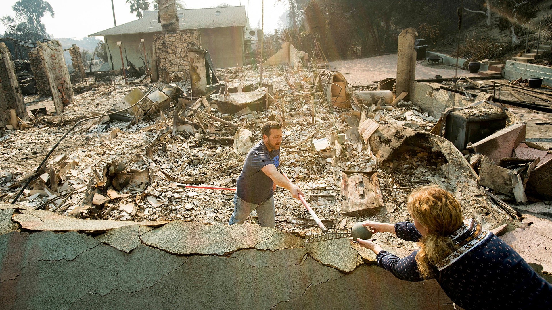 Paul Mattesich and his wife Erica Mattesich sift through rubble at his family's Ventura, California home following a wildfire, Wednesday