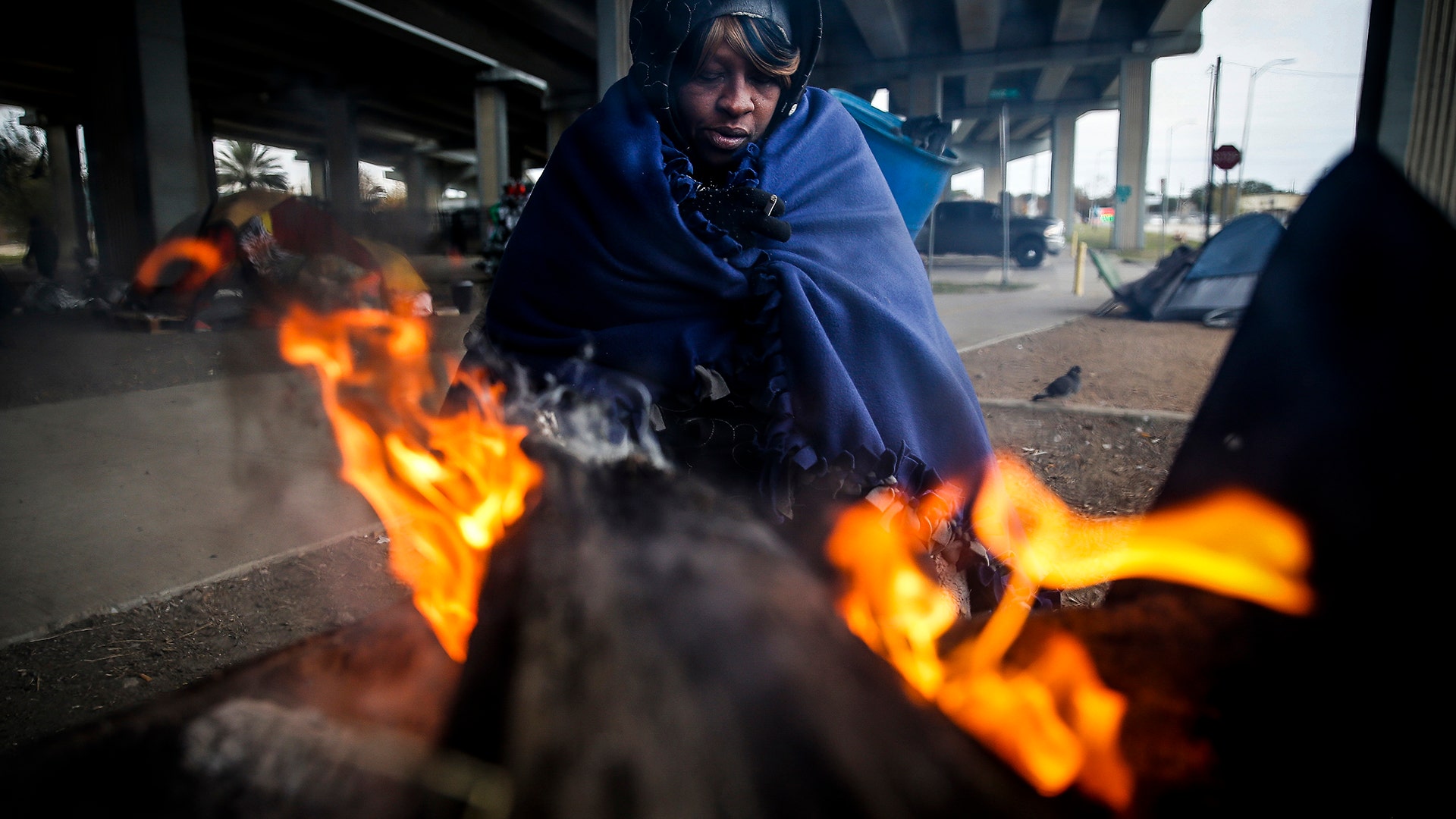 Tony Sampson, who received a blanket from Star of Hope's Love in Action van, tries to warm up by a fire under the Eastex Freeway  in Houston