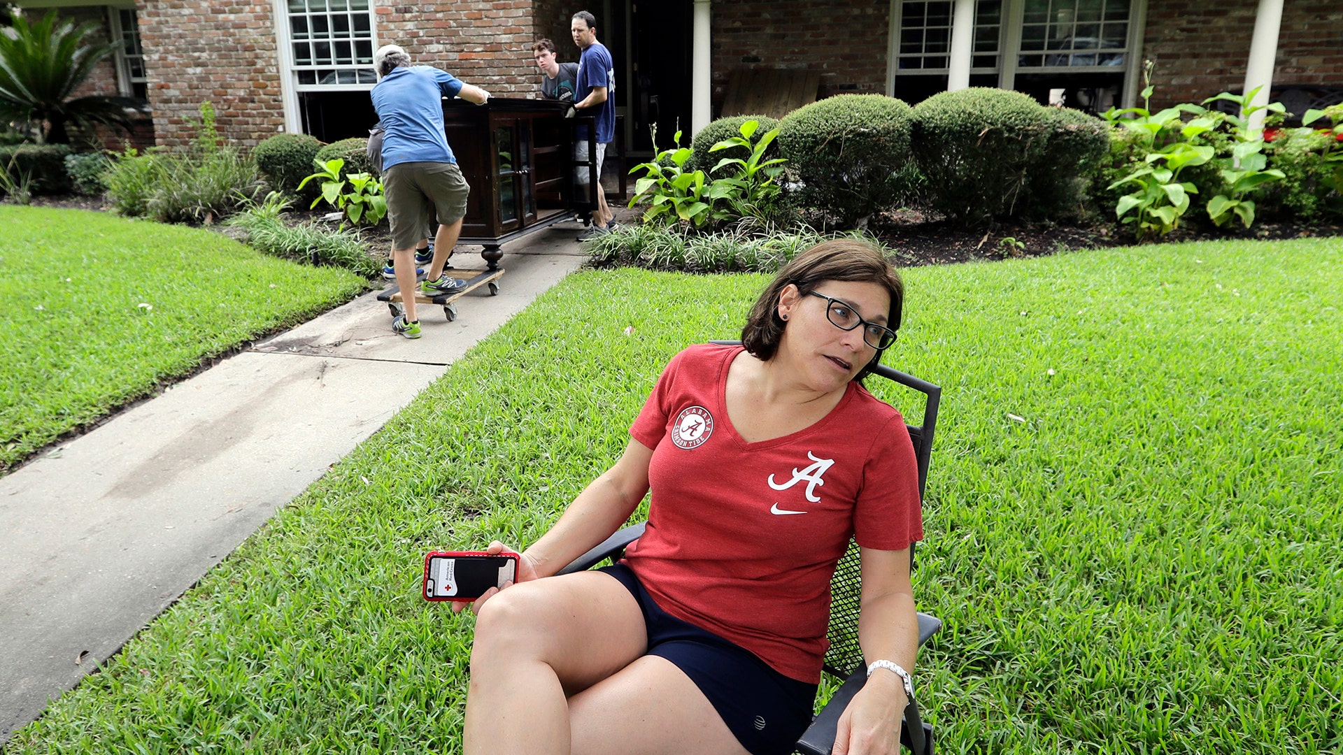 Natalie Hausman-Weiss sits on her front lawn as friends help remove furniture damaged by floodwaters in Houston, Wednesday